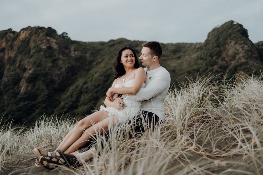 A romantic moment captured on a clifftop overlooking the ocean with tall grass swaying in the breeze.