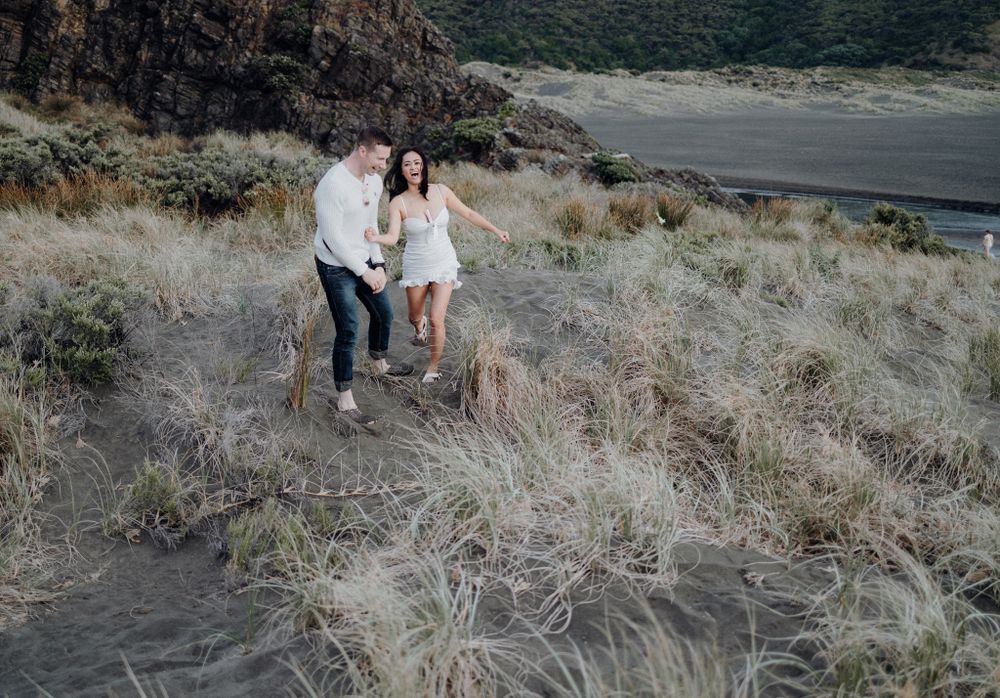 A couple walks along a scenic coastal trail with dramatic cliffs and ocean views in the background.
