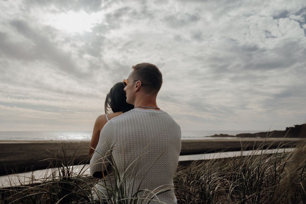 A tender embrace against a moody coastal landscape with dramatic clouds overhead.