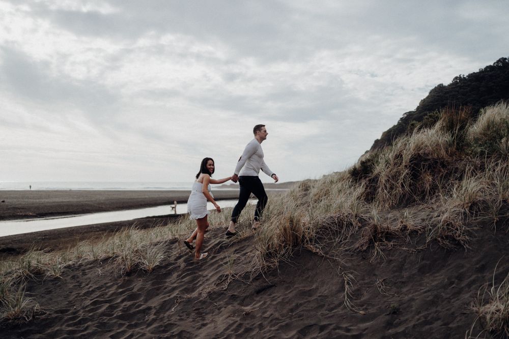 Two people climbing up a steep sandy hill against a cloudy sky.