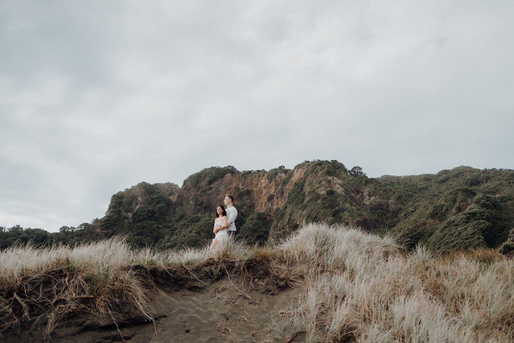 Two figures standing on a hilltop with dramatic cloudy skies behind them.