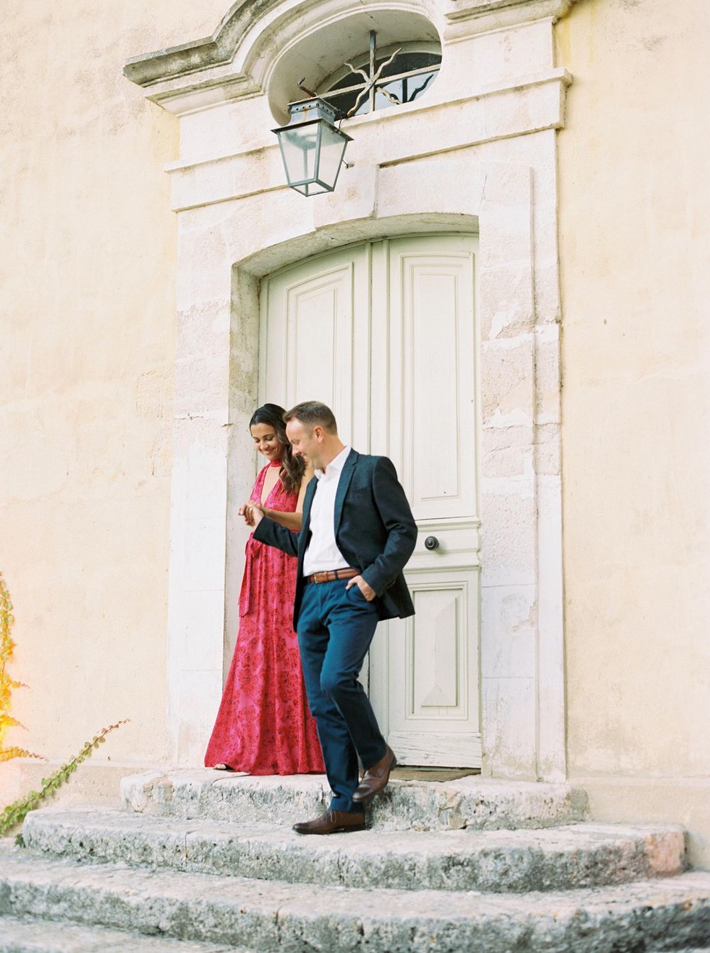 A couple, dressed as bride and groom, walk down stairs in front of a building at La Bastide de Ganay, Provence.