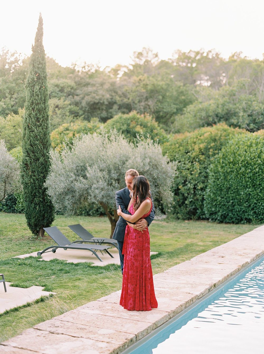 n Provence's La Bastide de Ganay, a bride and groom elegantly stand near a pool, both dressed in stunning red attire.
