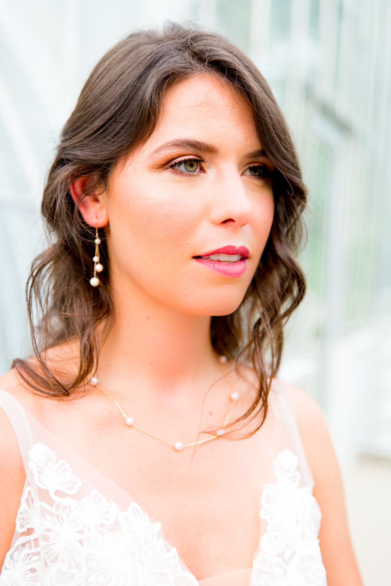 bride in hot pink lipstick, gold and pearl dangle earrings, and pearl and gold necklace stares off to the side at Krohn