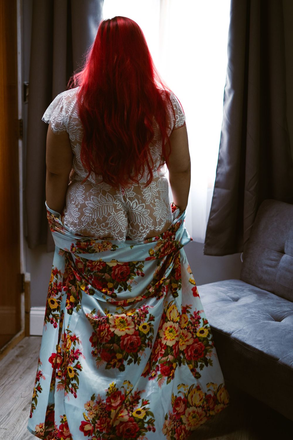 woman in bridal lingerie and floral bathrobe looking out the window, in a sexy pose with the robe framing her butt