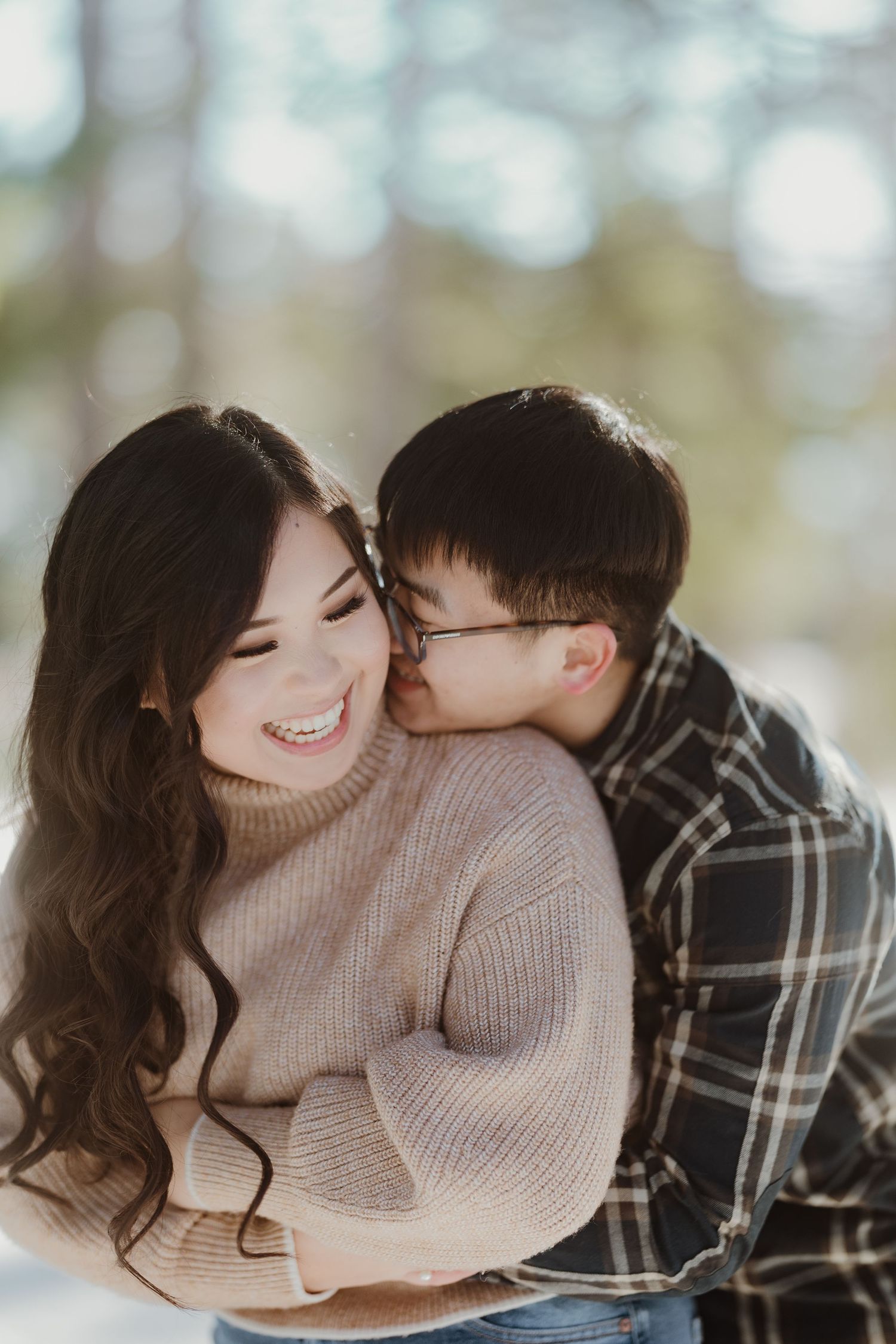 A tender winter photoshoot moment between a couple wearing cozy sweaters in the snow.