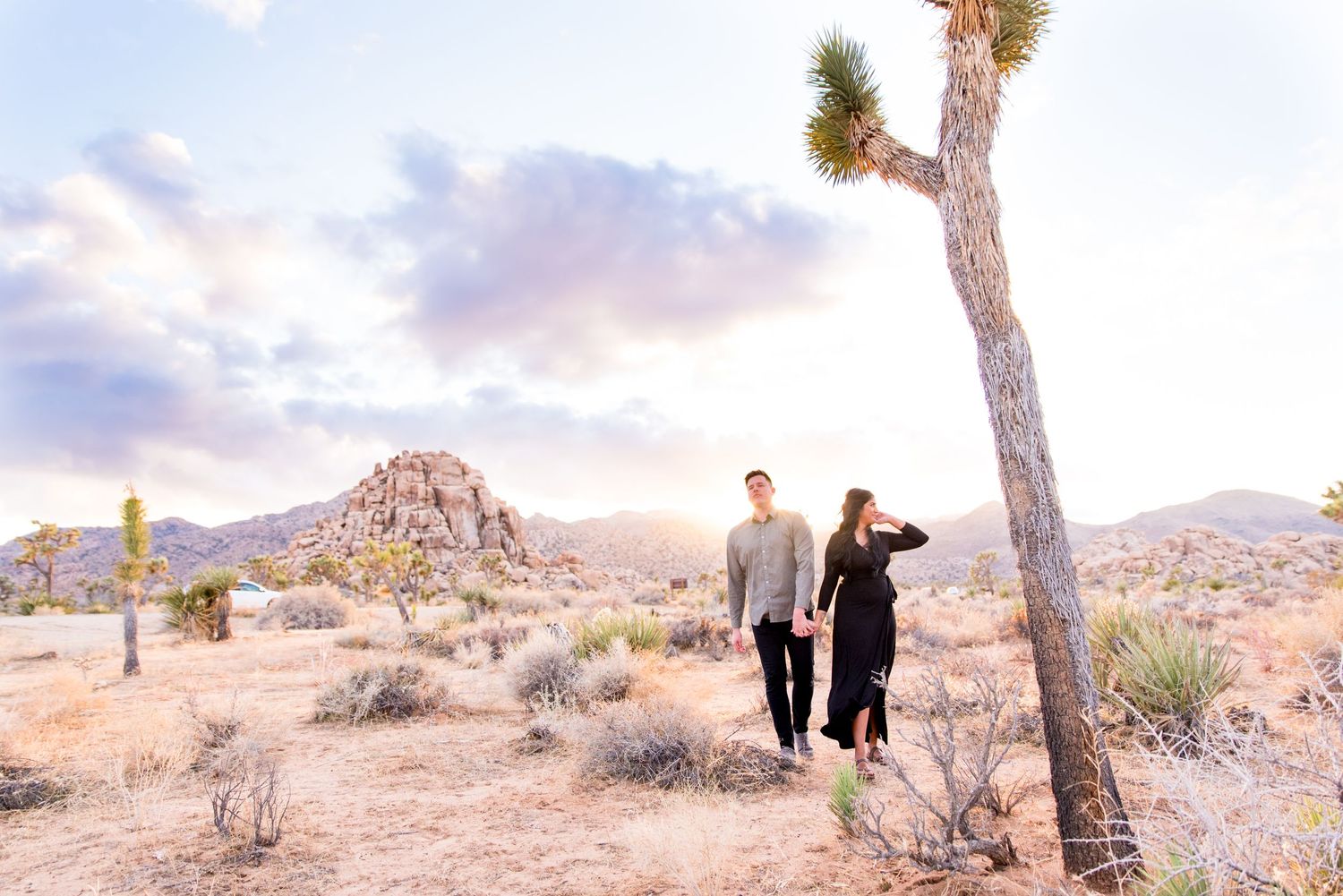 man and woman hold hands in Joshua Tree National Park under a blue and pink cloudy sunset