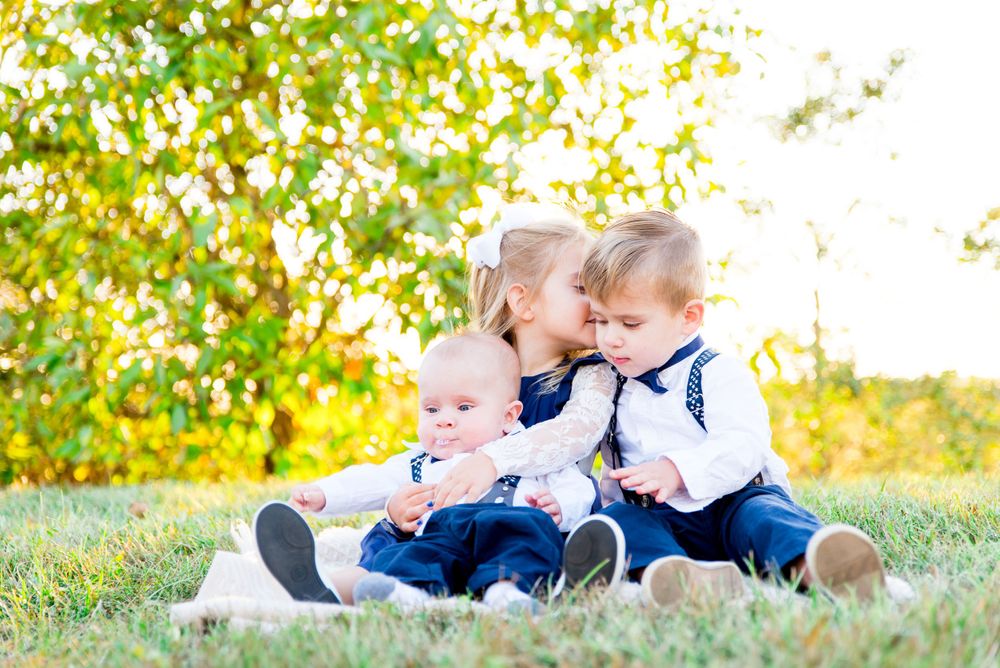 young girl kissing young brother on the cheek and holding baby brother at sunset in Millenium Park park