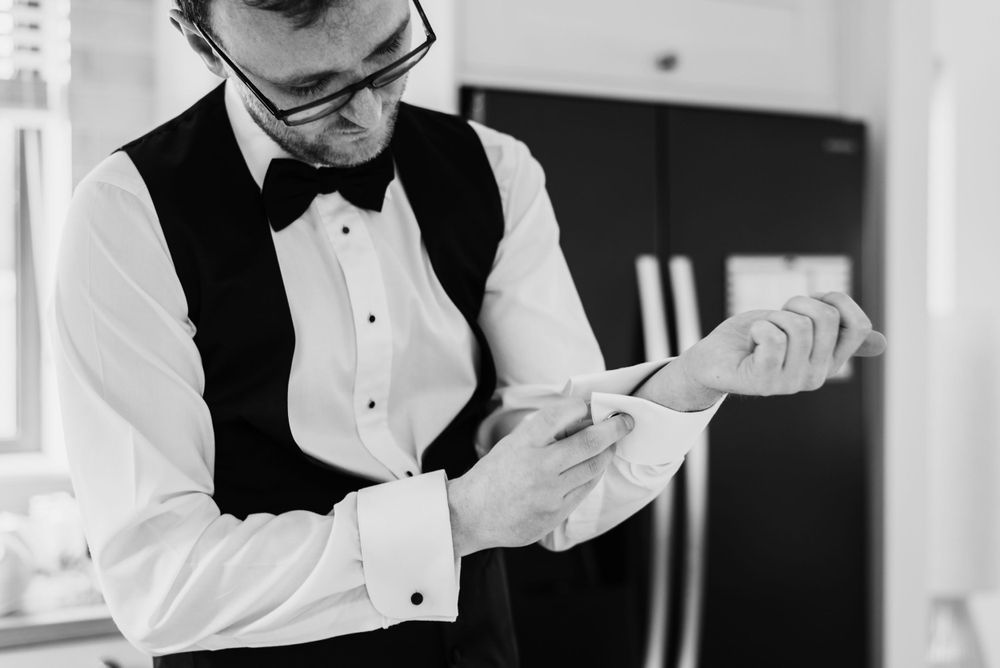 Black and white image of the groom fixing his cuff links.