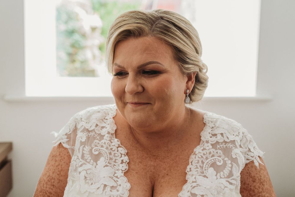 Head shot of the bride. showing the lace details on the top of her dress. She is smiling and looking to the side.