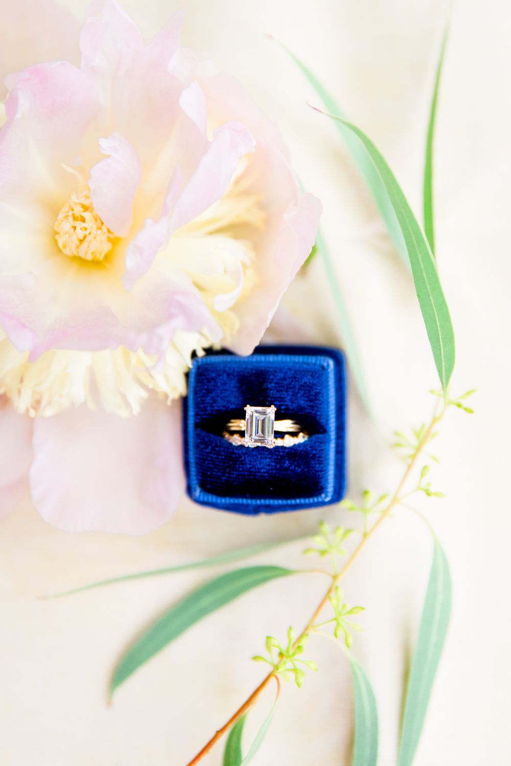 peony and green leaves surround blue ring box with emerald cut engagement ring and wedding band from Richter Phillips