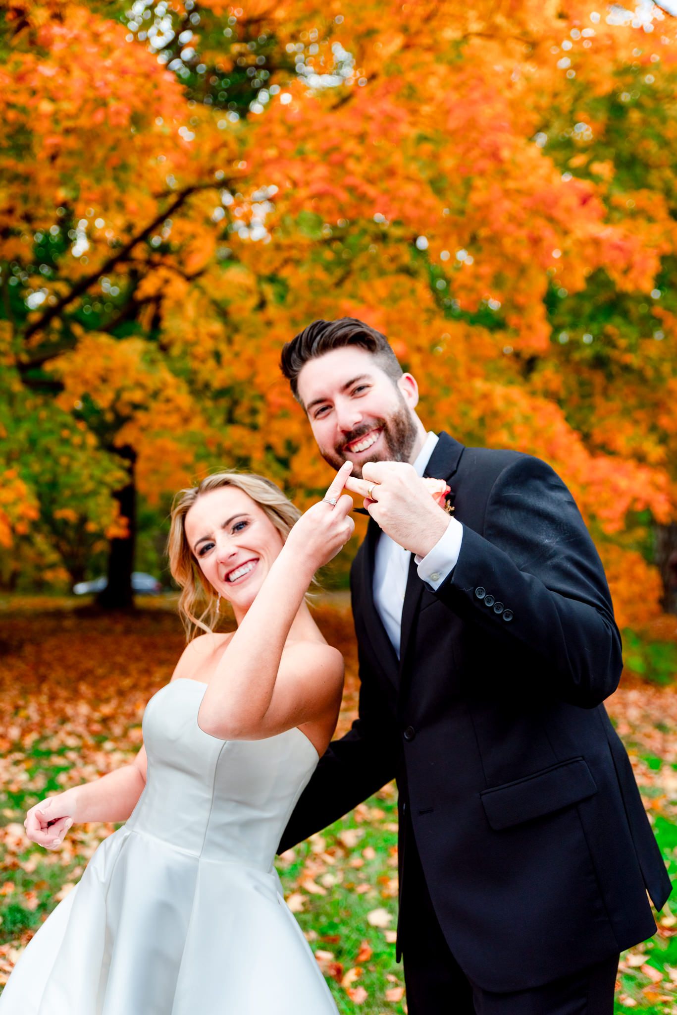 bride and groom hold up ring fingers in front of bright orange tree