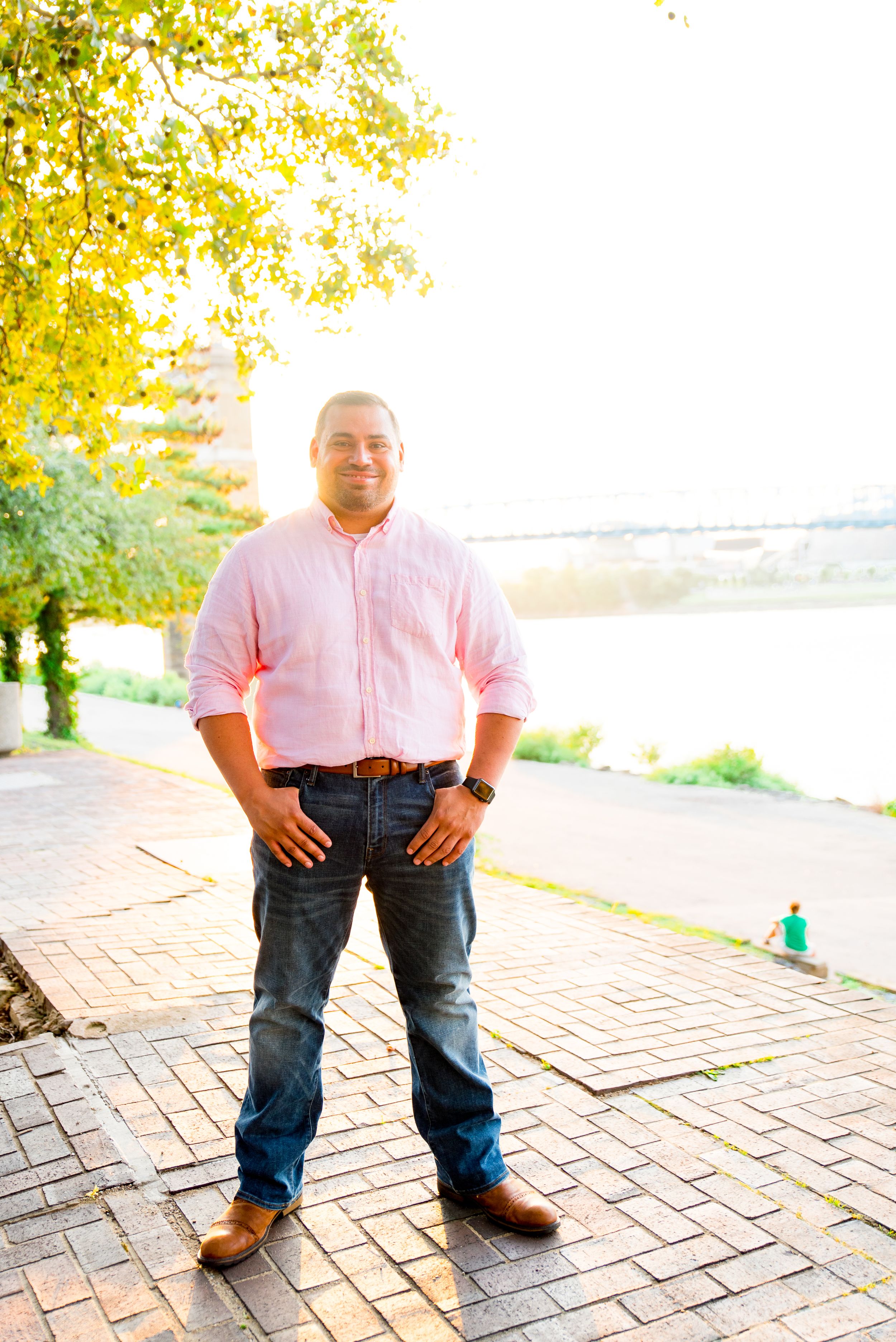man in light pink long sleeve button down and dark blue jeans smiles in front of Roebling Bridge