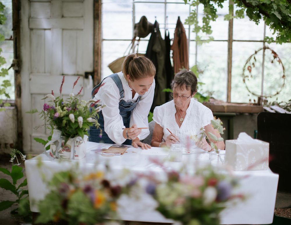 A woman wearing blue dungarees teaches an art class inside a large Victorian greenhouse