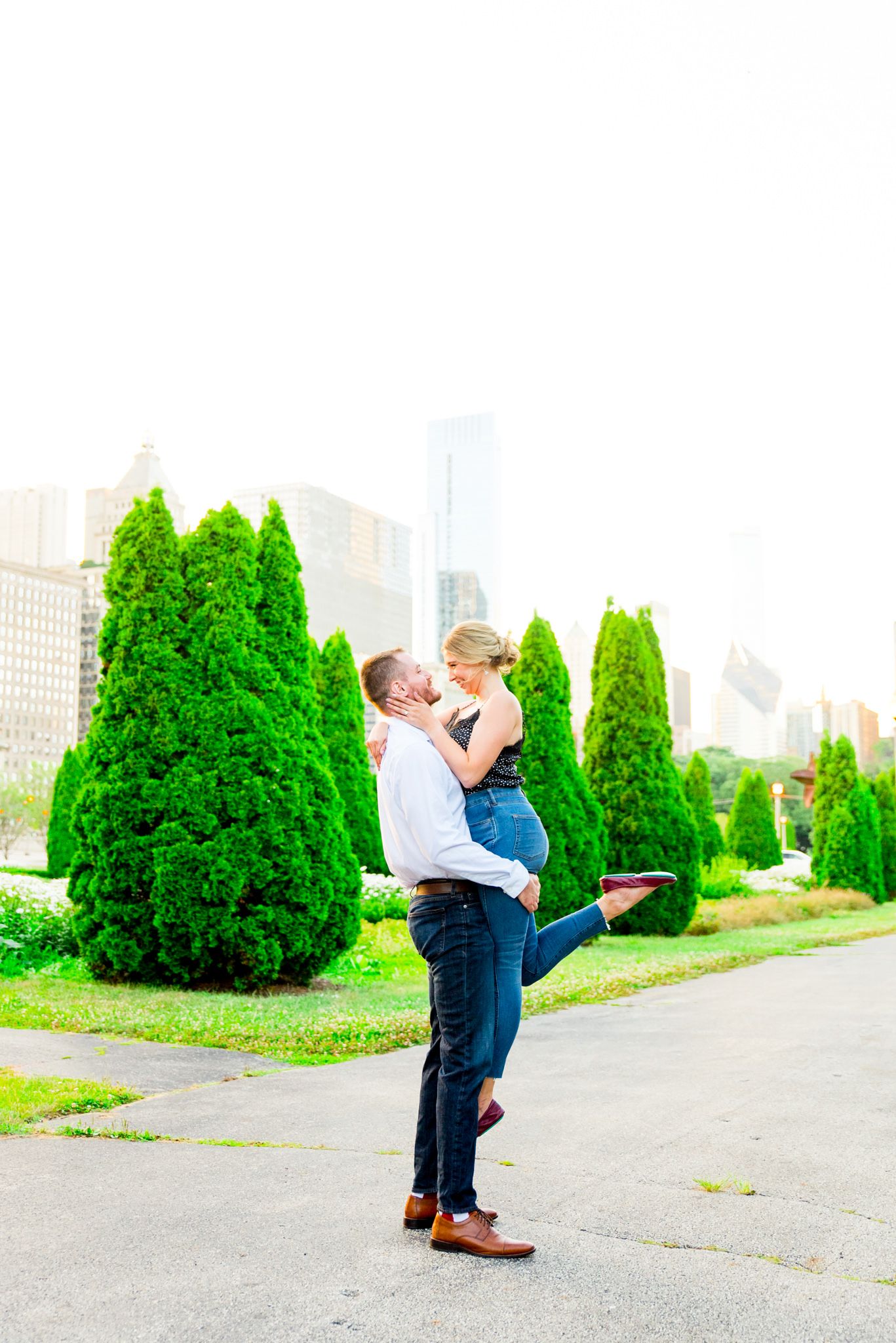man picking up his fiance smiling at each other in the middle of Grant Park for chicago sunset engagement pictures