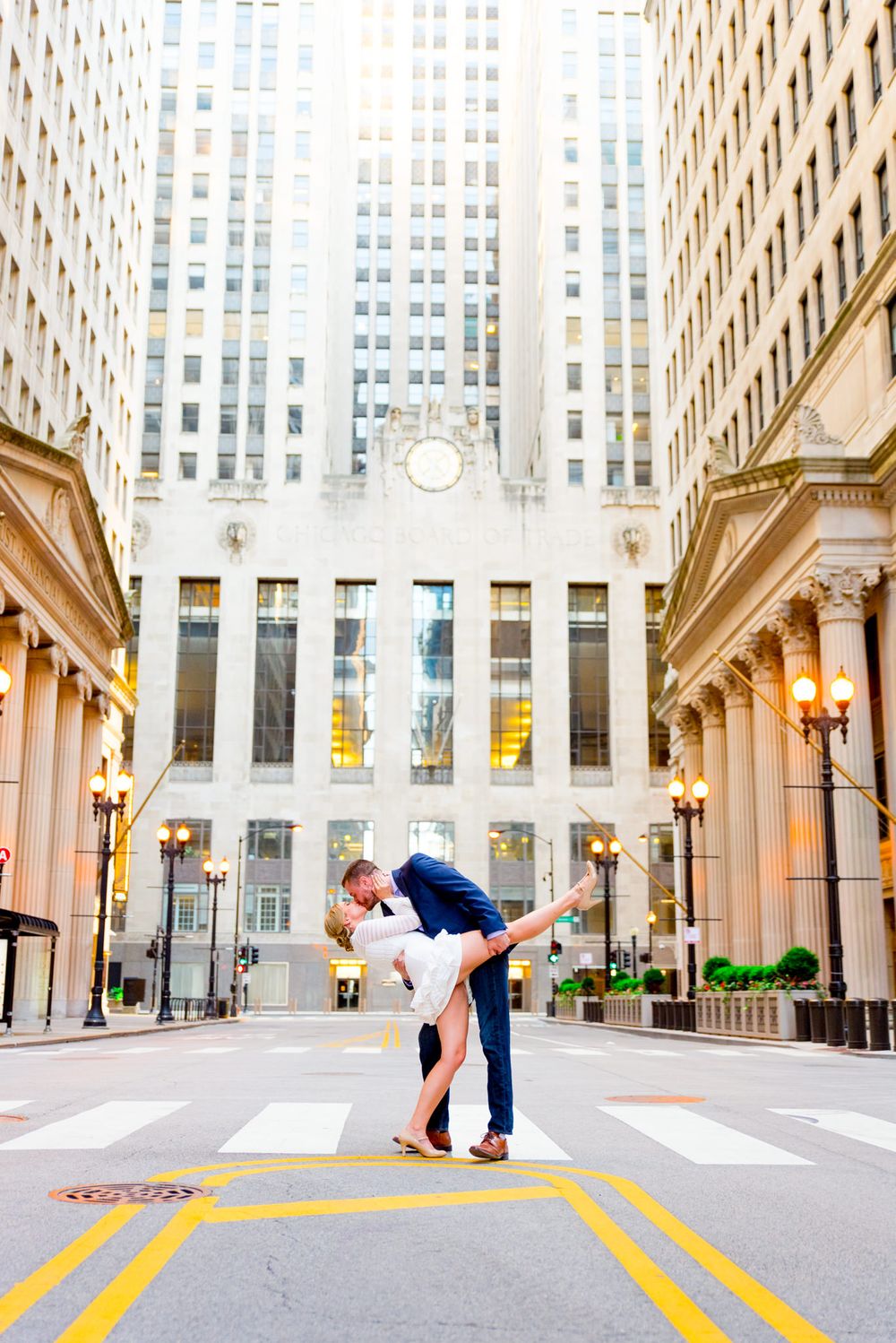 man in navy suit dipping woman in white dress in front of Chicago Board of Trade for engagement pictures