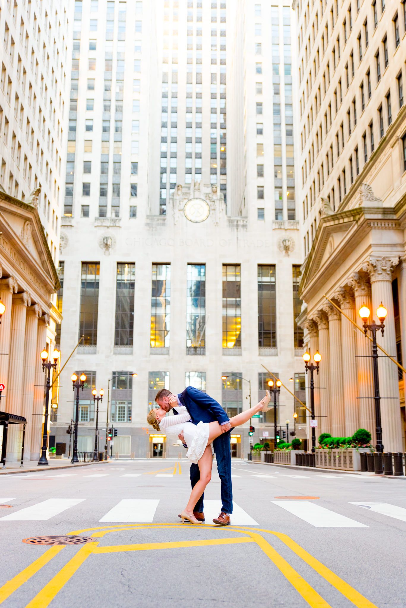 man in navy suit dipping woman in white dress in front of Chicago Board of Trade for engagement pictures