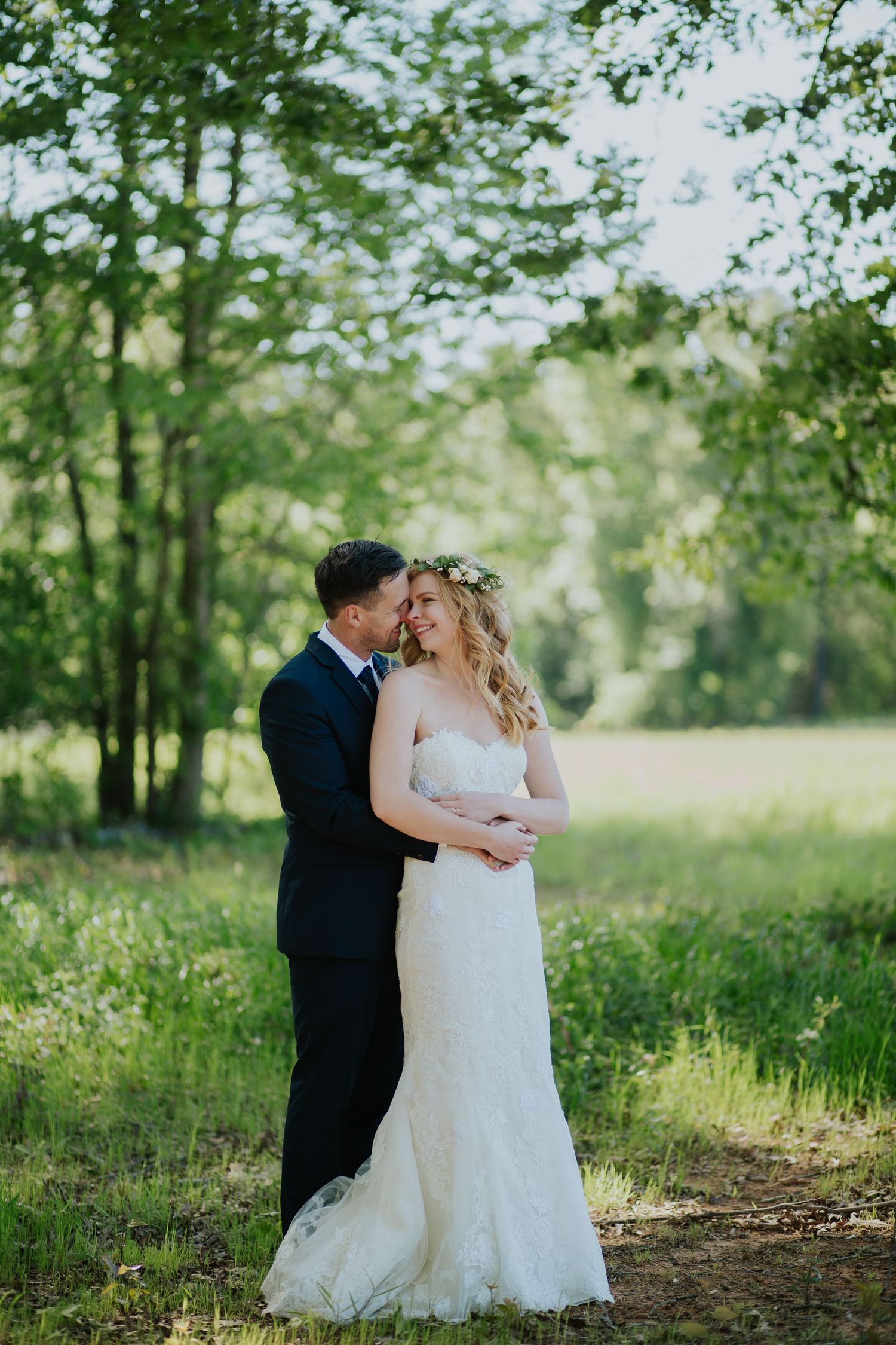 A bride and groom share an intimate moment in a sun-dappled forest clearing.