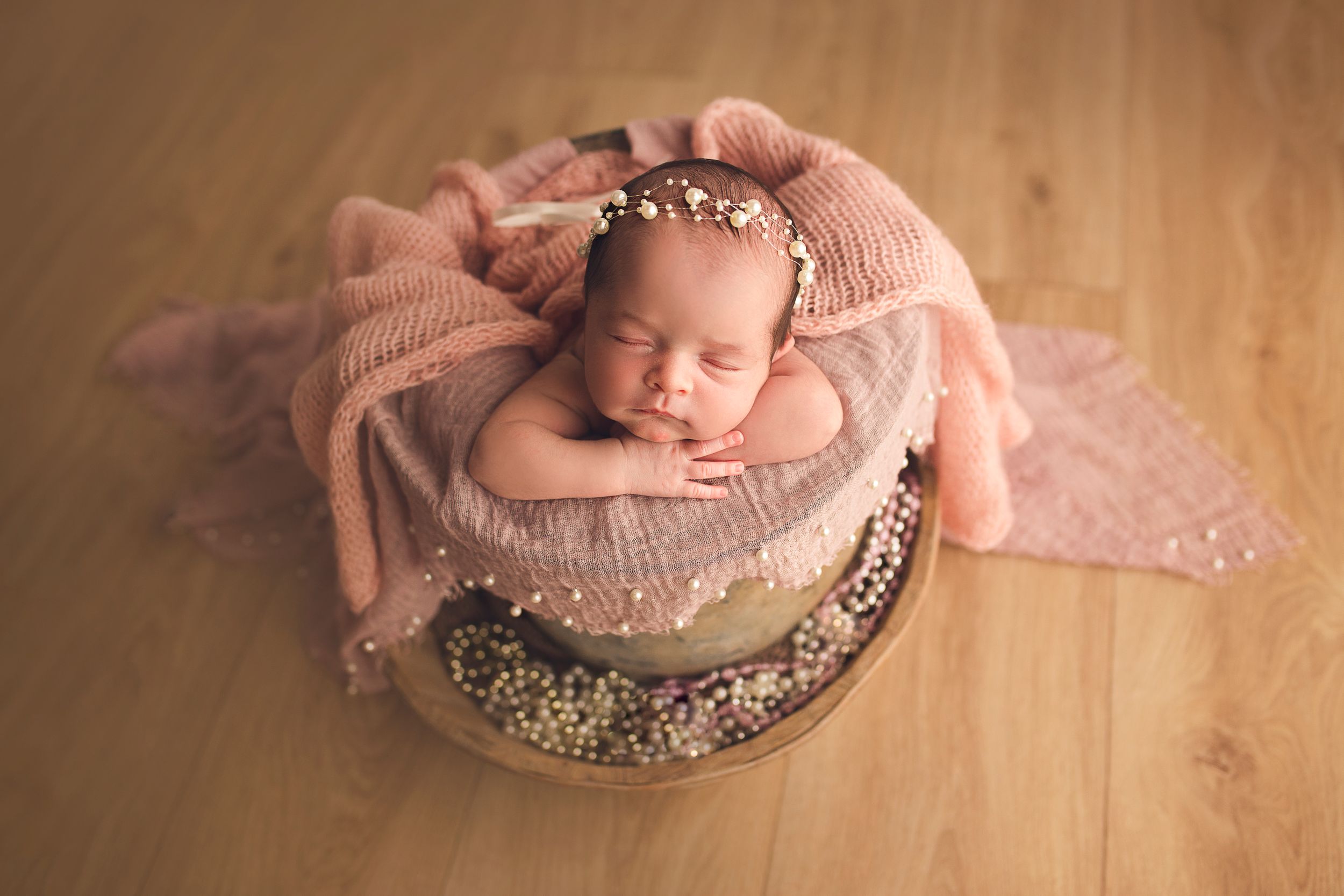 Newborn baby girl with pearl headband sleeping in a bucket pink colored