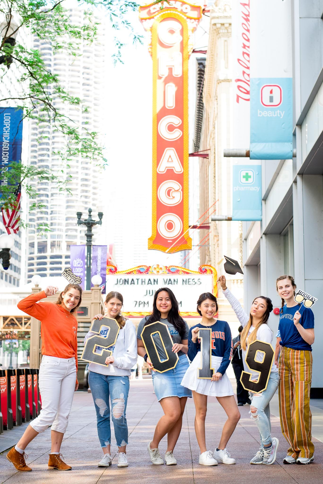 six senior girls in front of the Chicago Theater sign for Chicago senior pictures holding up 2019