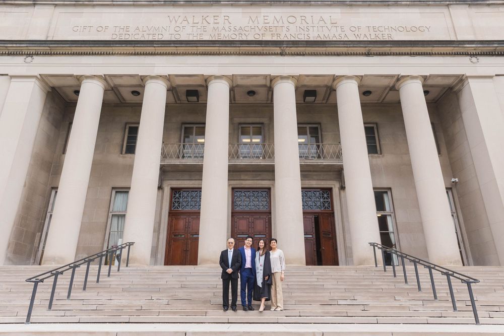 Three people pose on the steps of a classical university building with columns.