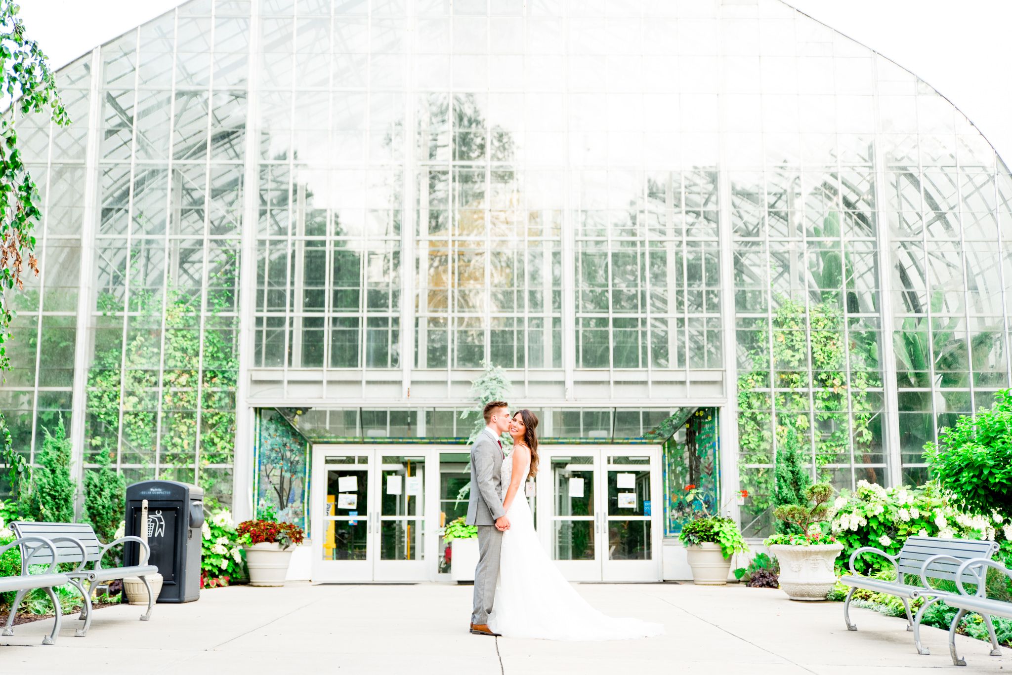 bride and groom hold hands in front of Krohn Conservatory in the summer