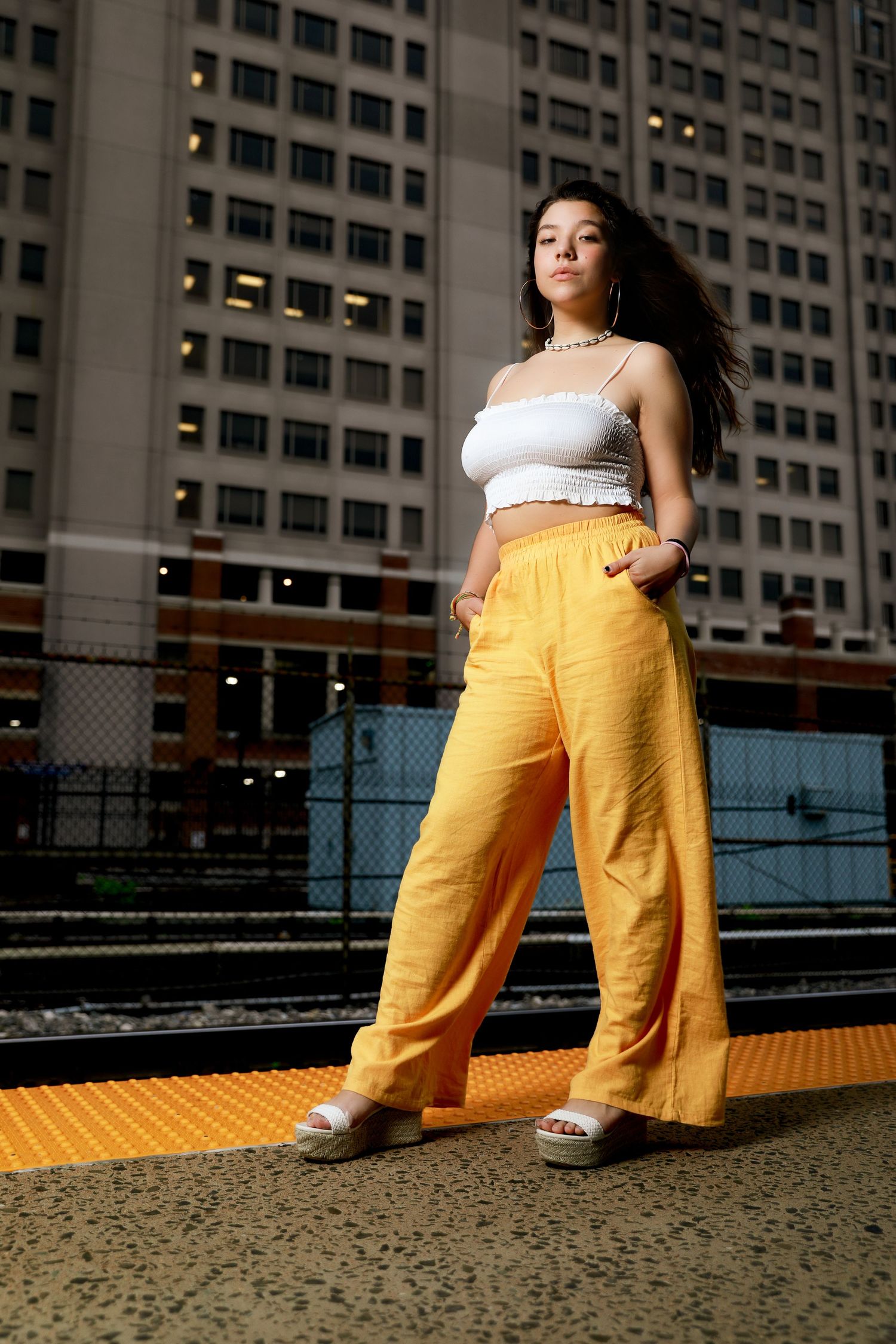 Urban fashion look with yellow pants and white crop top against city architecture.