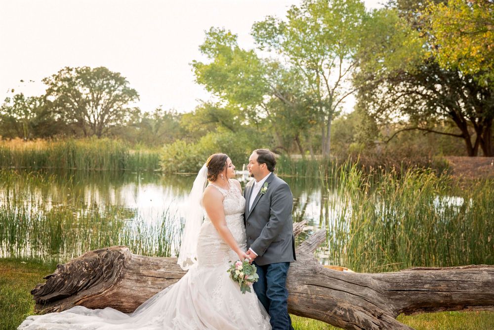 Bride and groom on a log at the pond at Fallen Oaks Estate