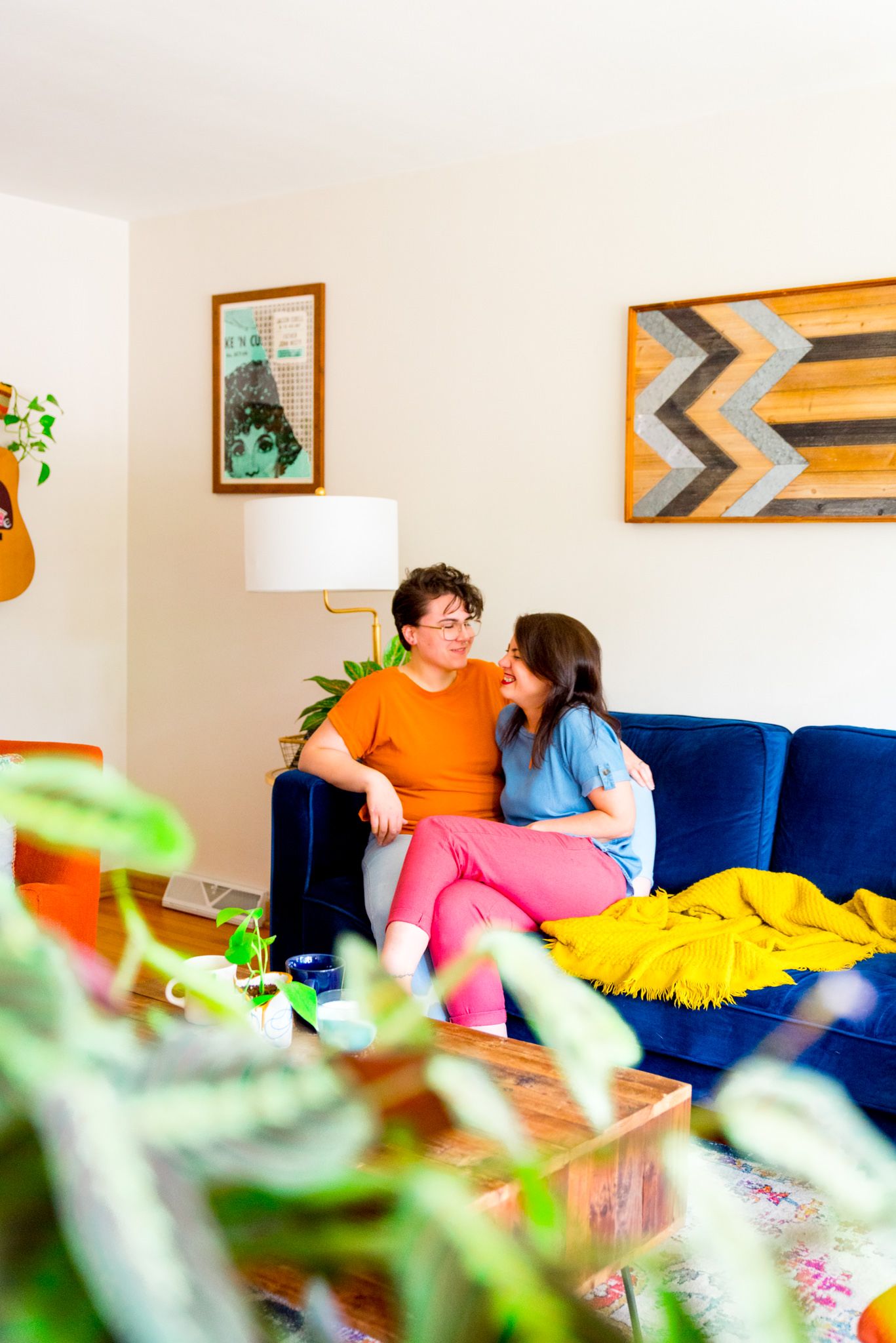 women in pink orange and blue clothes sit and laugh on blue couch in their living room for Chicago LGBT couples pictures