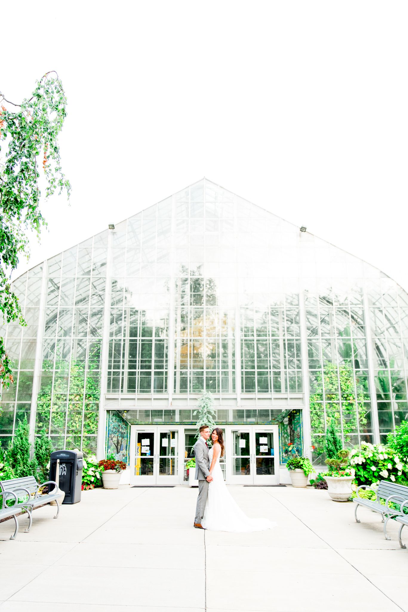 bride and groom hold hands and kiss cheek in front of Krohn Conservatory summer wedding