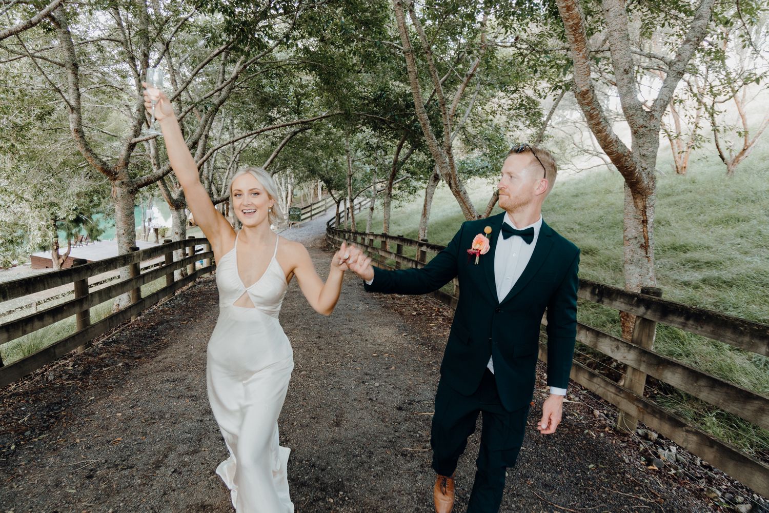 Newlyweds walk hand in hand along tree-lined path celebrating their marriage.