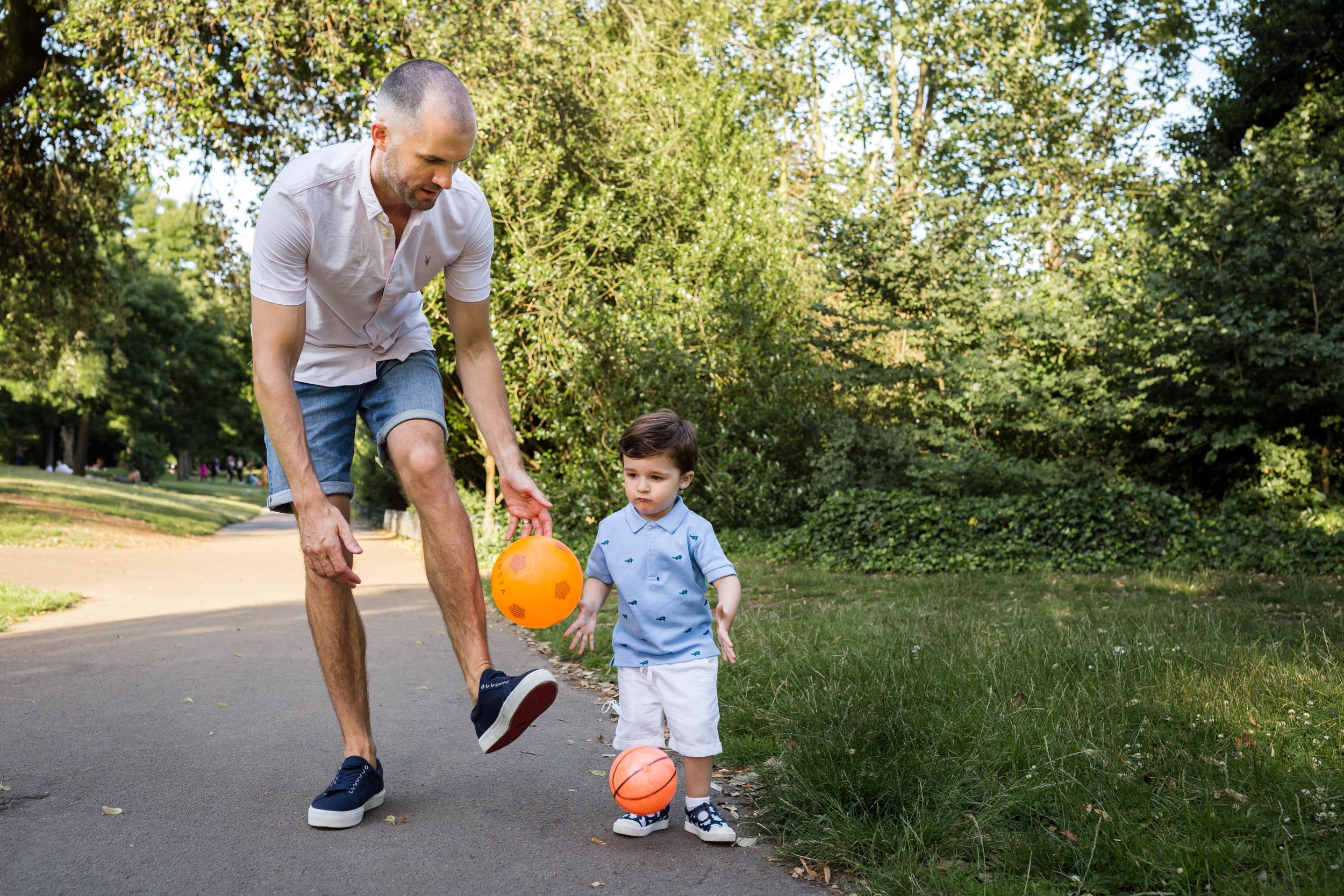 father and son kicking orange football in Victoria park east London