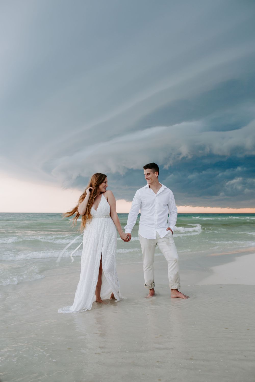 man and woman holding hands on the beach as the woman smiles at the man