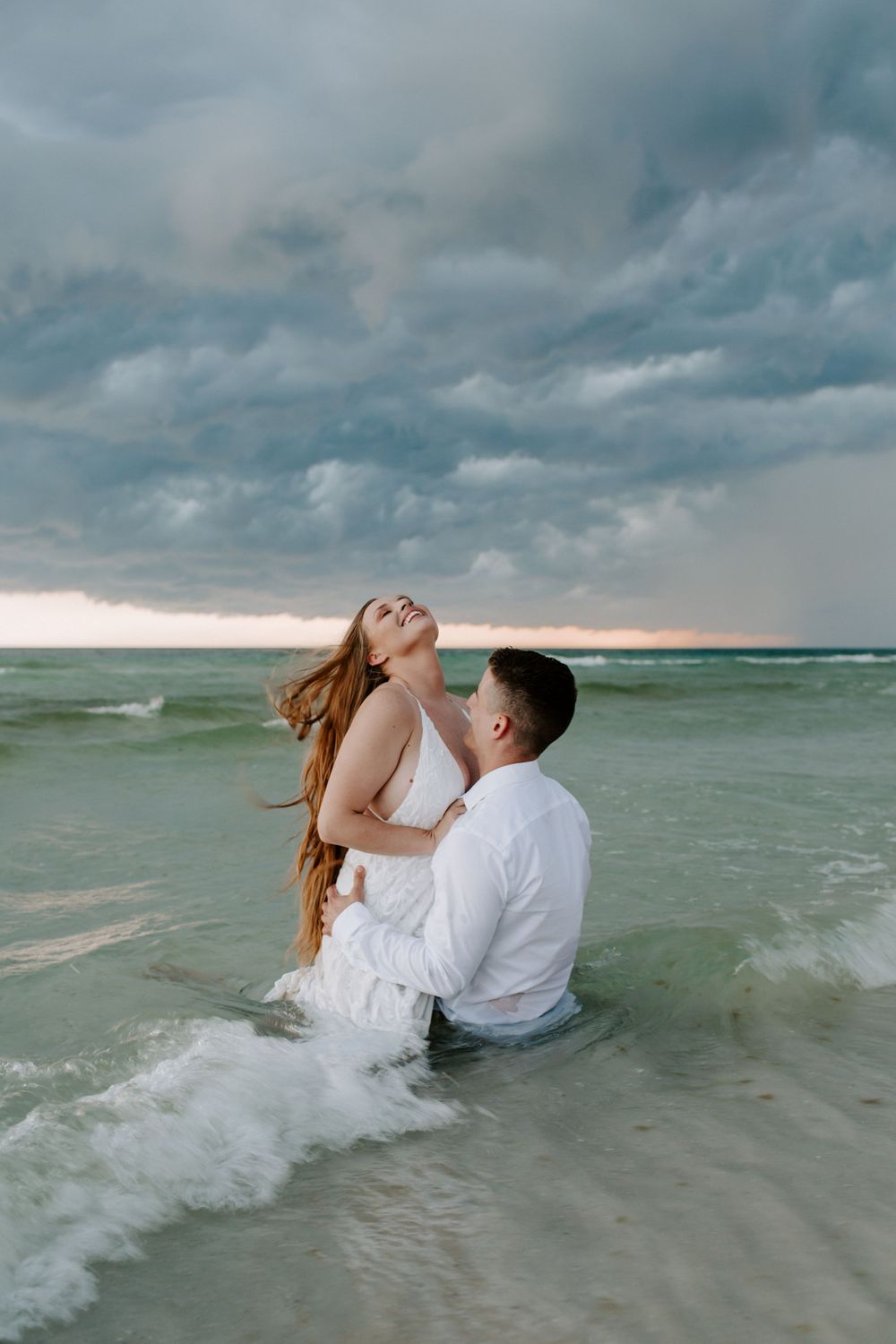 woman sitting on her partner as she throws her head back with a summer storm rolling in
