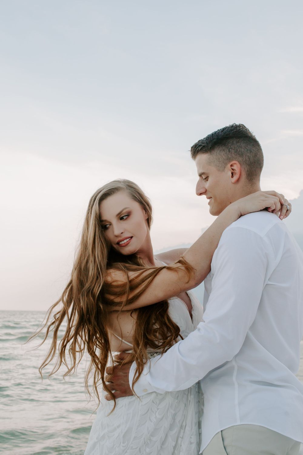 man and woman with their arms around each other as the man looks at her and she looks down at the ground