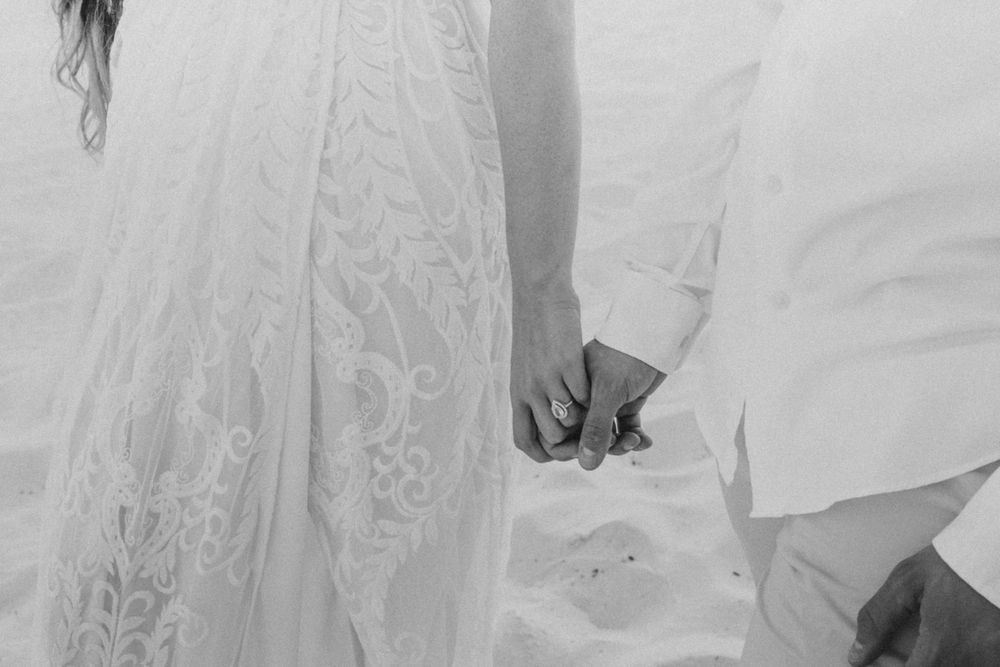 newly wed couple holding hands walking the beach