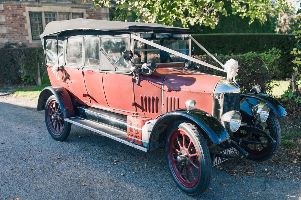 Vintage red touring car from early 1900s with canvas top parked on driveway.