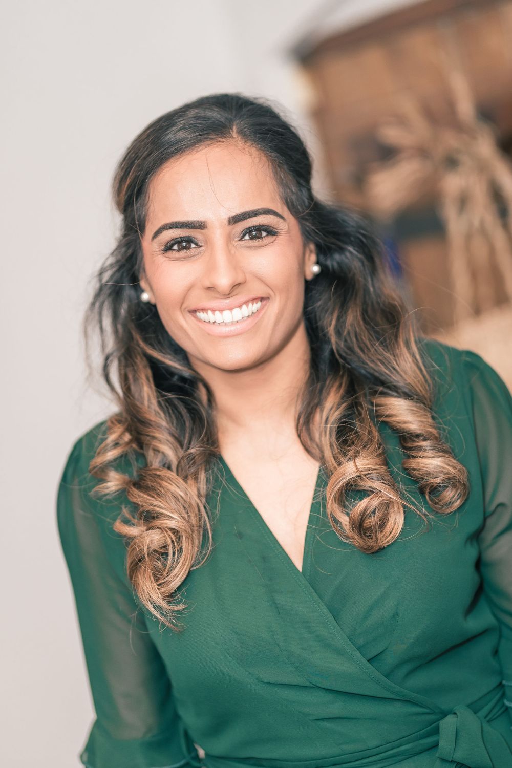 Woman in emerald green wrap dress with ombre curled hair smiles at camera.