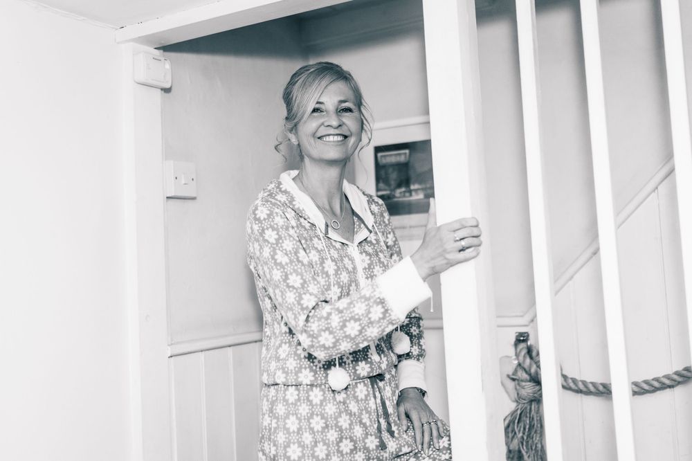 Black and white photo of woman in polka dot dress smiling by staircase.