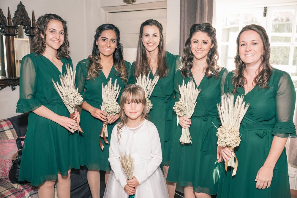 Wedding party wearing matching emerald green dresses with white dried flower bouquets.
