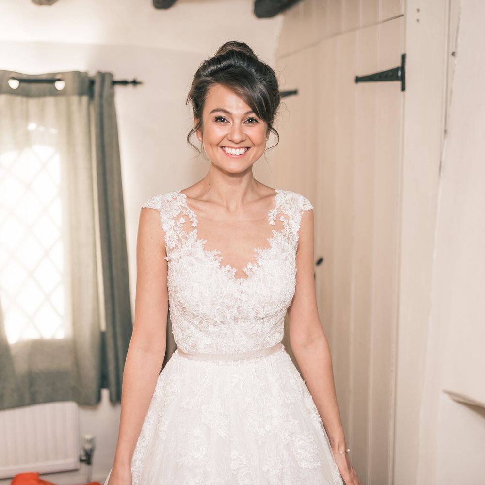 Bride wearing delicate lace wedding gown smiles in natural light.