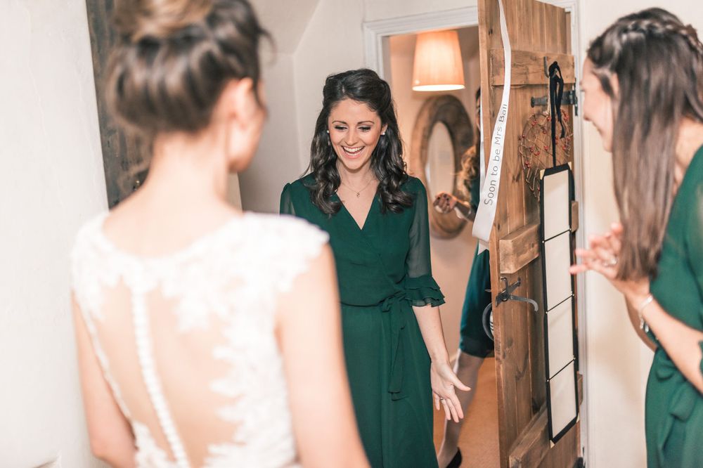 Bridesmaids in green dresses admire bride in white gown.