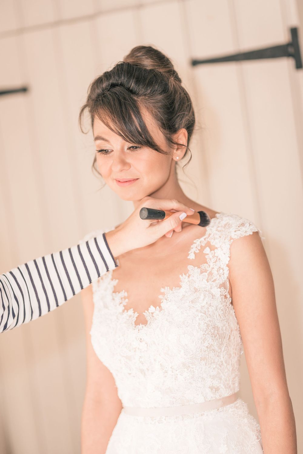 Final makeup touches being applied to bride in lace wedding dress.