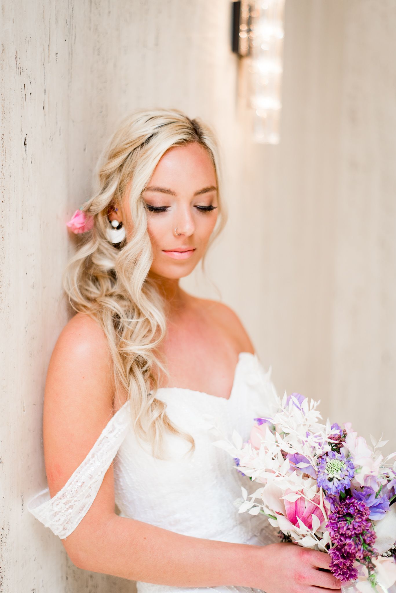 blonde bride with messy braid leaning on marble wall at pink purple white wedding bouquet