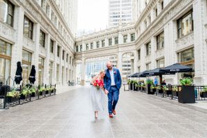 couple in navy suit and glittery dress with red bouquet walking under Wrigley building at Chicago Elopement