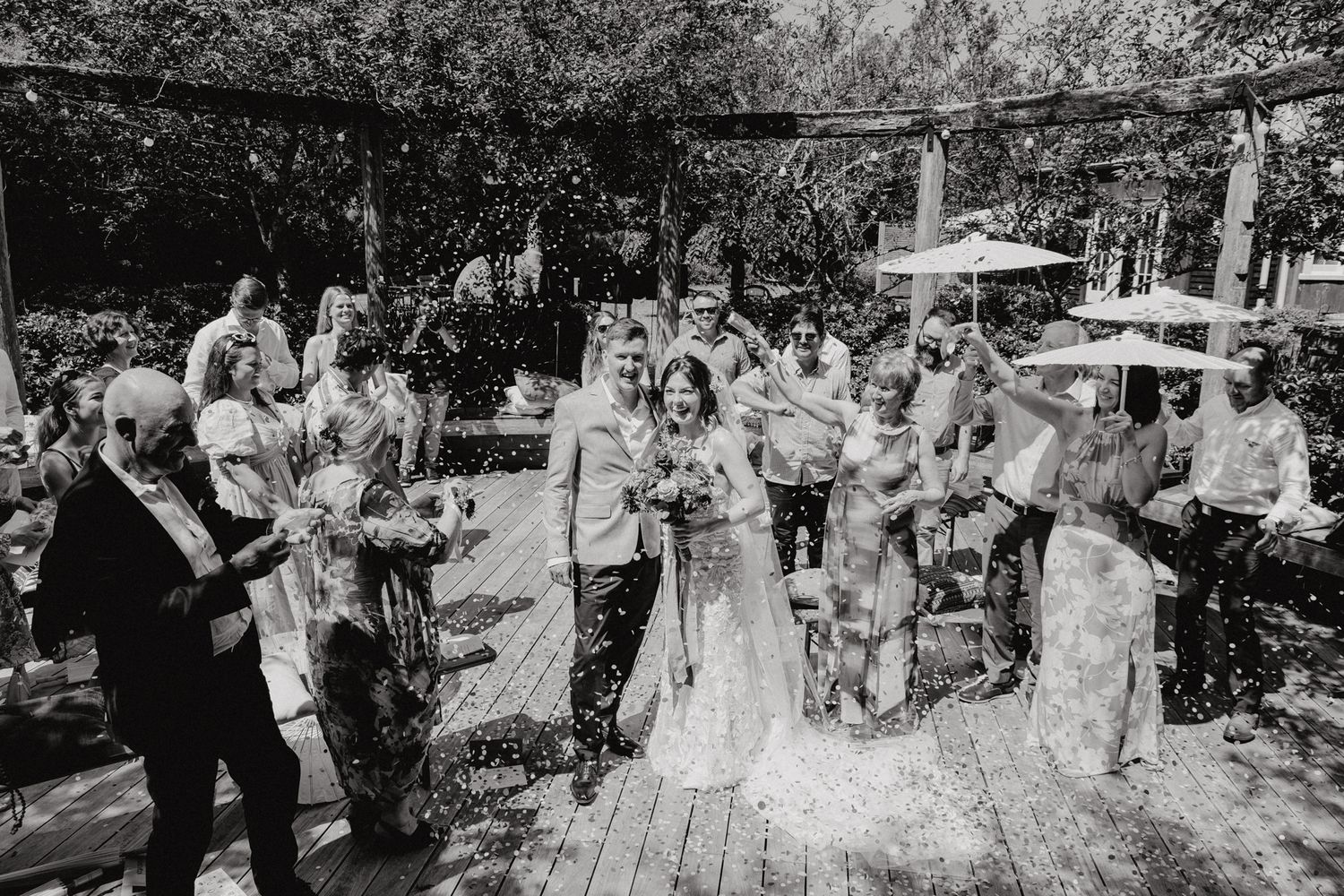 A black and white photo capturing a celebratory moment during an outdoor garden wedding ceremony.