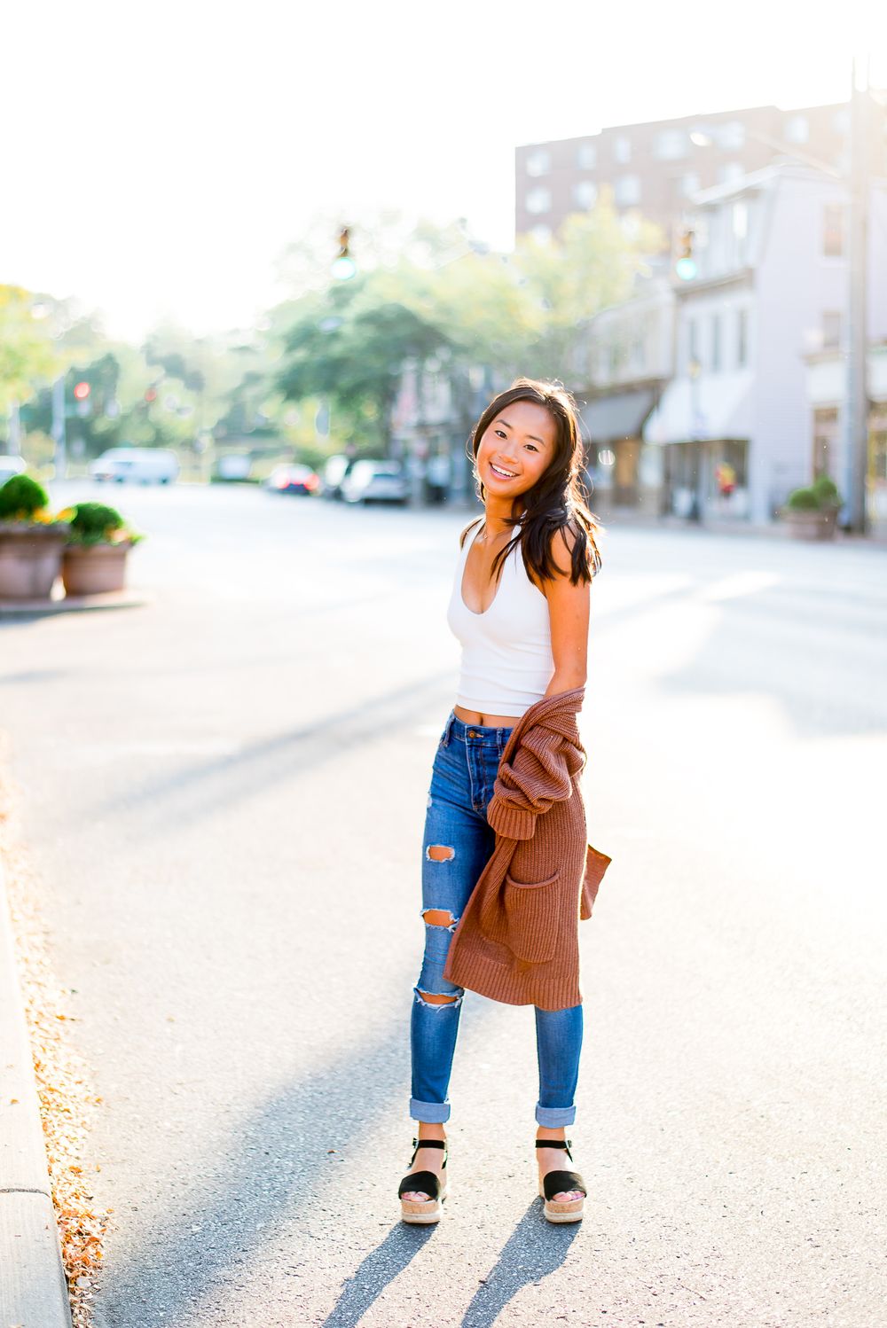 high school senior in a tank top and brown cardigan standing in the street at sunrise