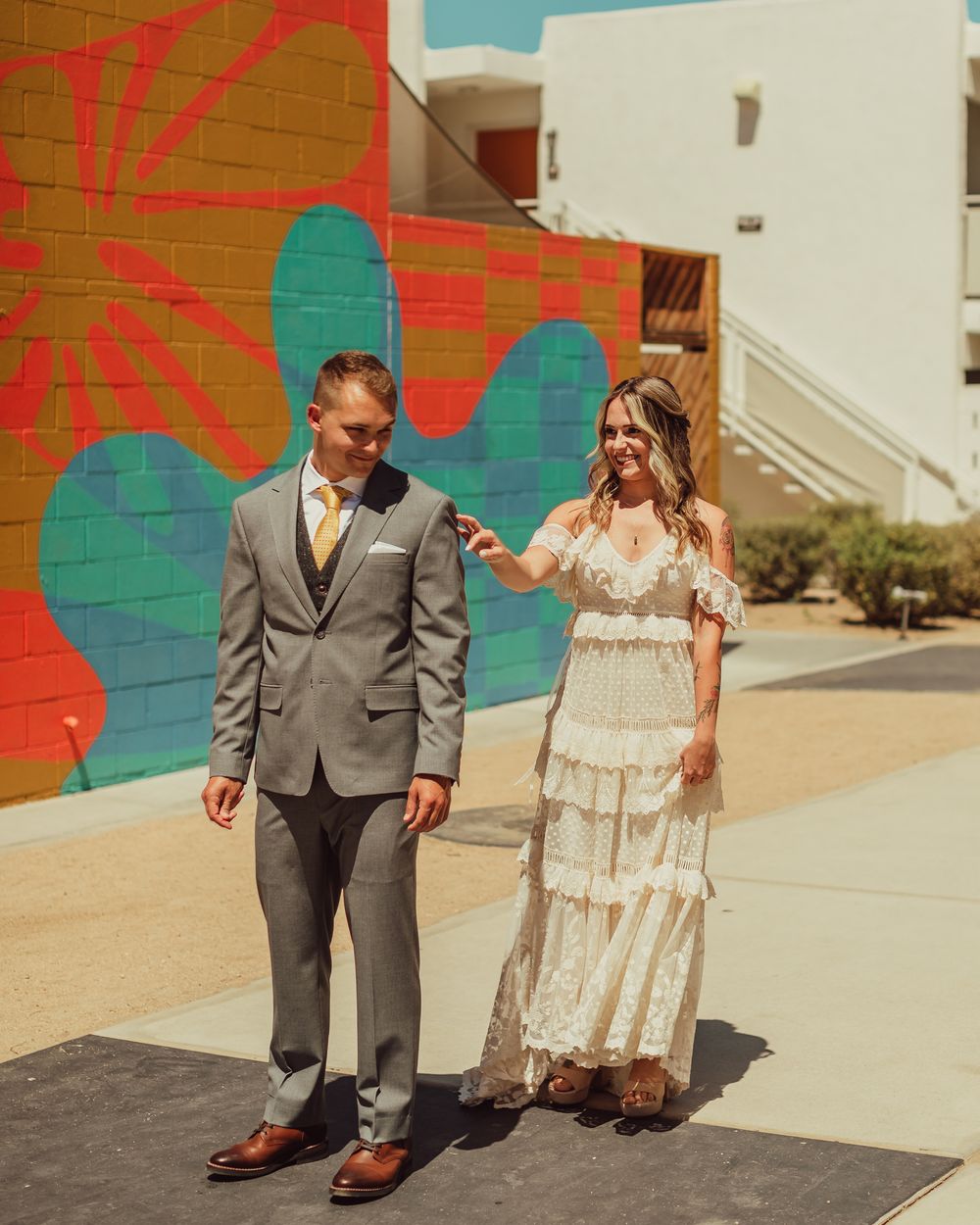 A couple in wedding attire poses together against a colorful mural wall with green and red geometric patterns at the ACE Hotel