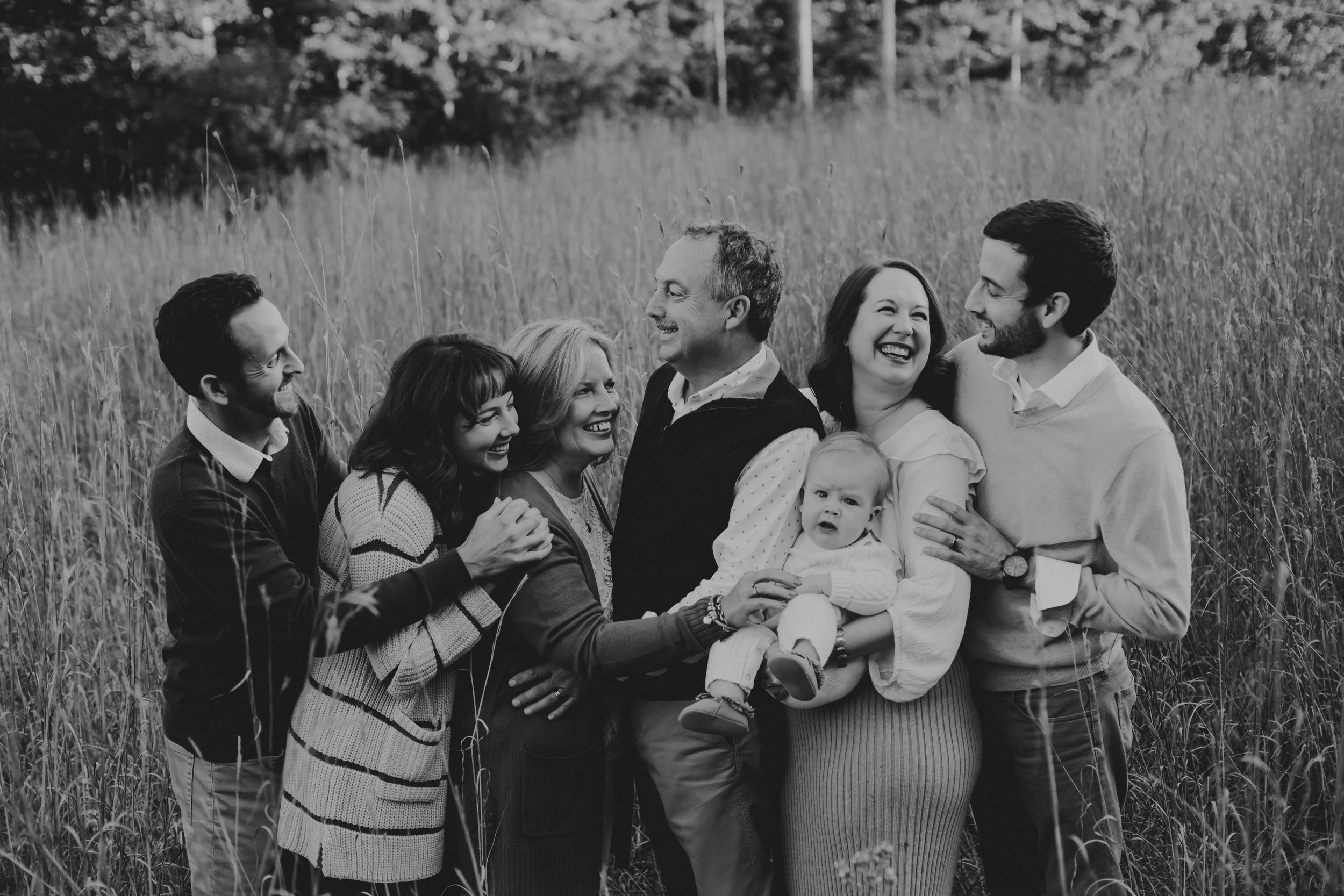 Black and white photo of all six adults with the baby laughing and smiling together in a field.