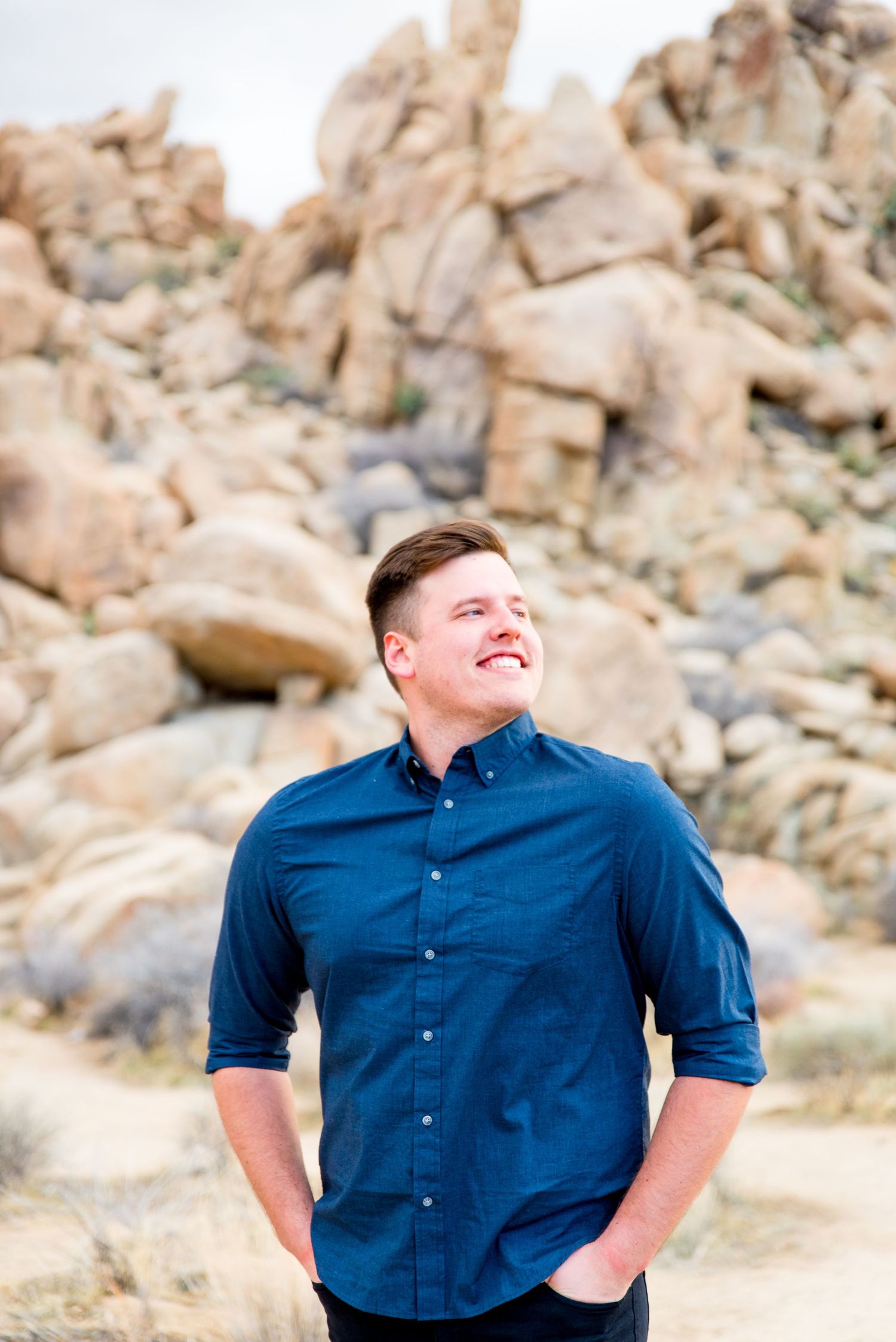 man in blue button down shirt looks to the right and smiles in front of rocks at Joshua Tree National Park